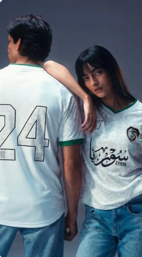 Young man wearing white Syrian football jersey on a basketball court at sunset